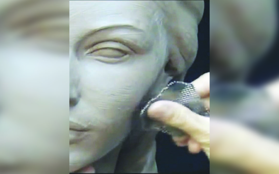Uno scultore all’opera  definisce i lineamenti del volto di argilla di una statua