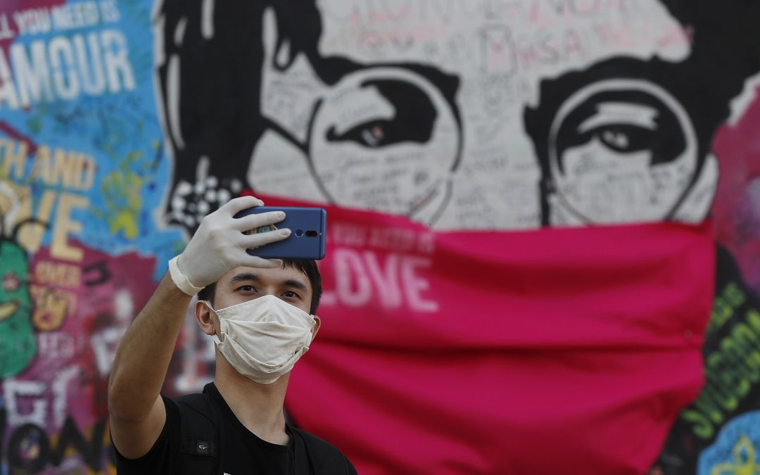 Un ragazzo scatta un selfie davanti a un murale dedicato a John Lennon