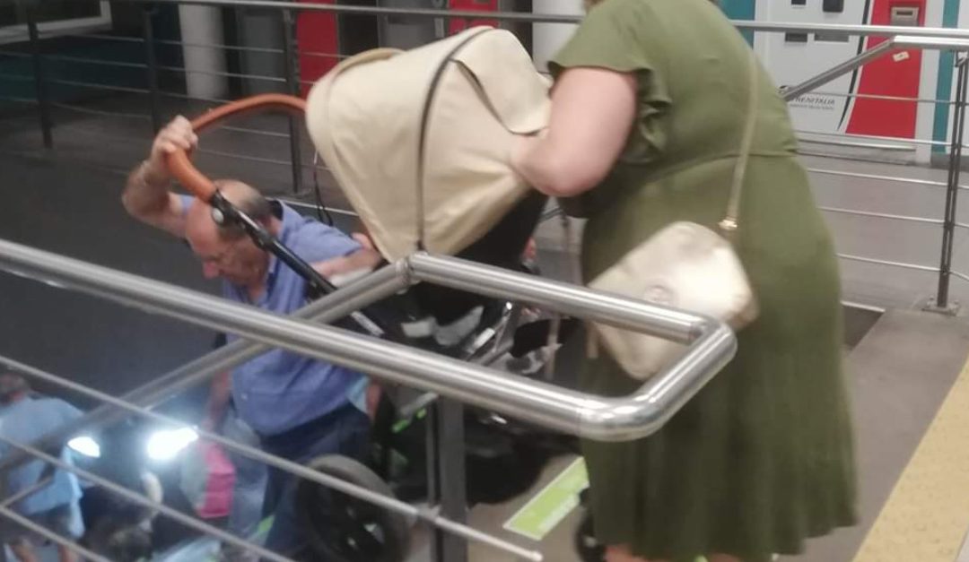 Due viaggiatori si arrangiano a trasportare i pesanti bagagli sulla scala della stazione di Paola