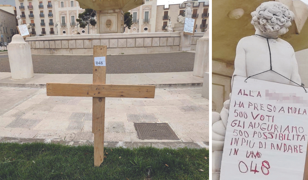 La croce piantata nel prato della piazza e uno dei manifesti affissi a Mola contro la consigliera regionale Parchitelli