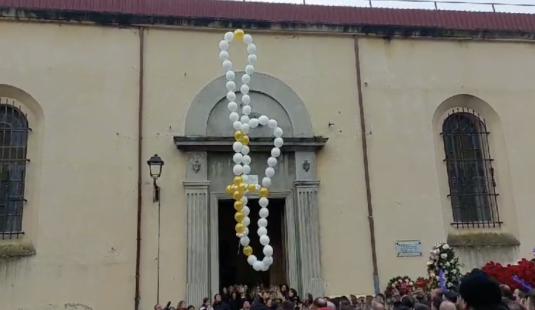 I palloncini uniti a formare una corona del rosario lasciati volare in cielo davanti alla chiesa