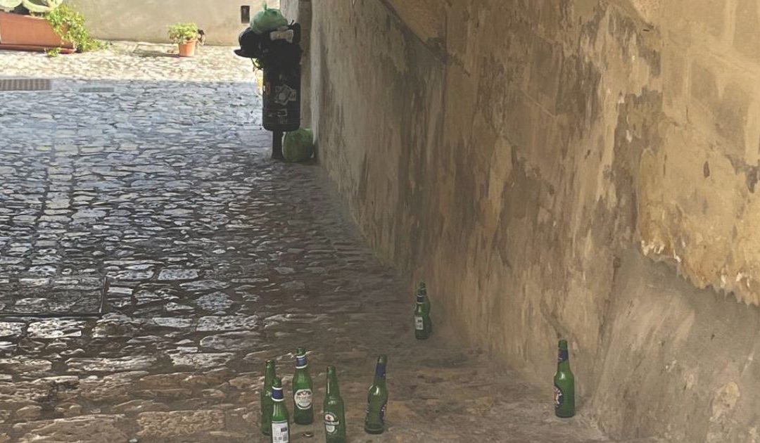 Un cestino stracolmo sullo sfondo e bottiglie sulla strada di accesso per i Sassi